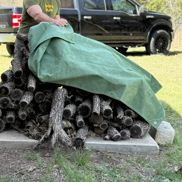 Green 10' x 12' canvas tarp covering stacked logs from outdoor weather exposure