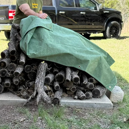 Green 8' x 12' canvas tarp covering stacked woodpile storage from weather exposure